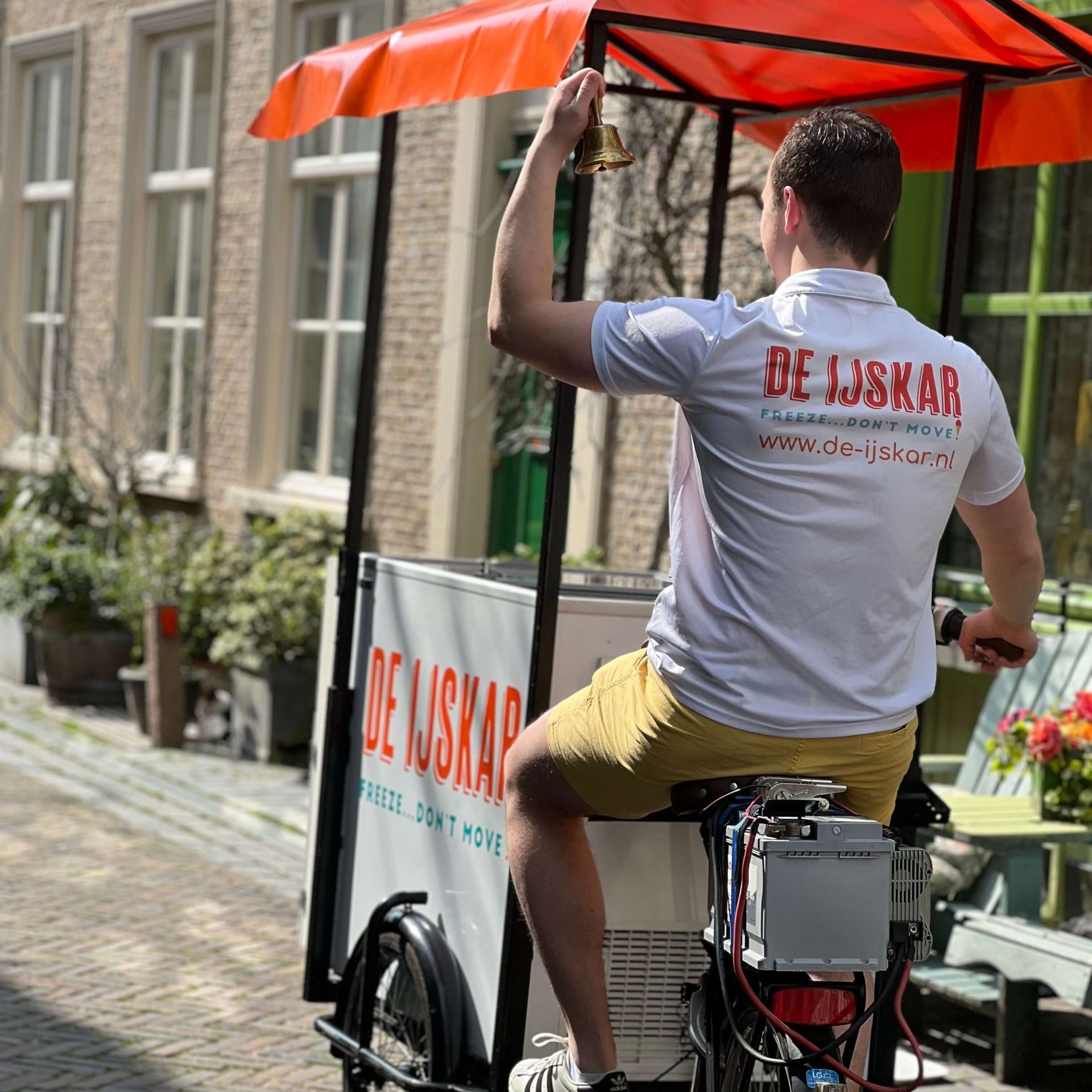Ijscoman luidt de gouden bel vanaf de ijskar-bakfiets in een oude binnenstadstraat