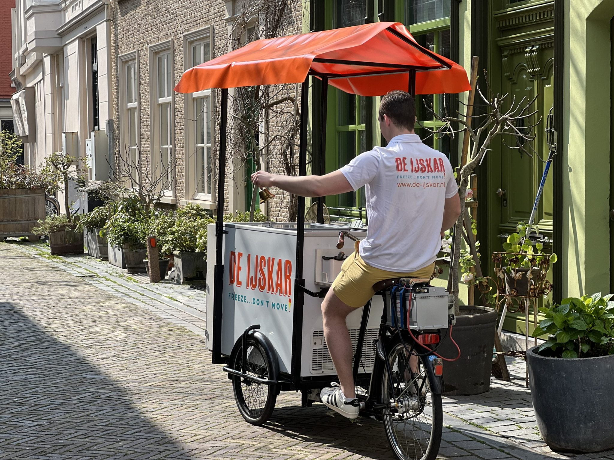 Ijscoman rijdt met de ijskar-bakfiets door een geplaveide straat en luidt de bel