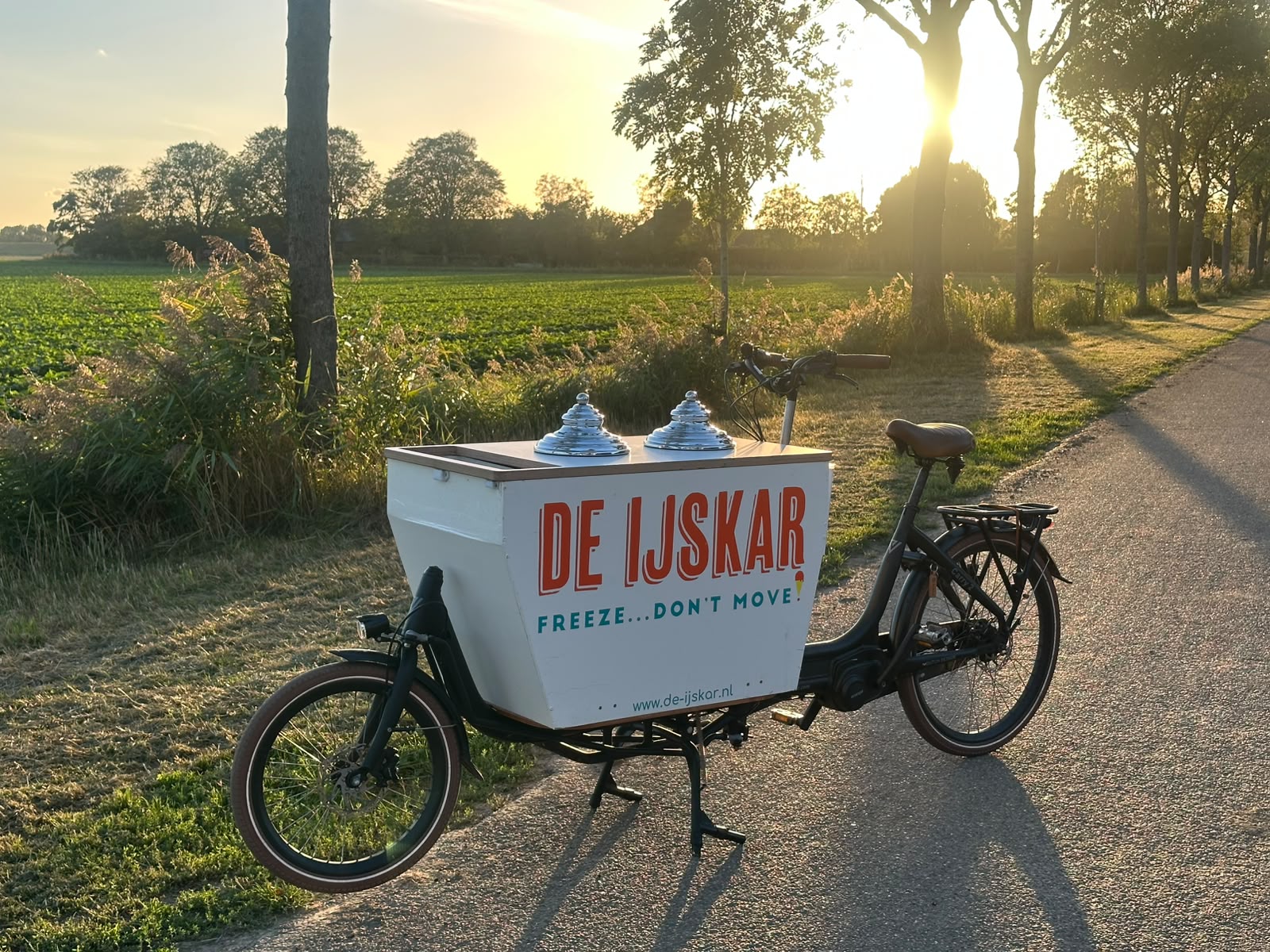 De IJsfiets bij zonsondergang op een landweggetje langs de velden