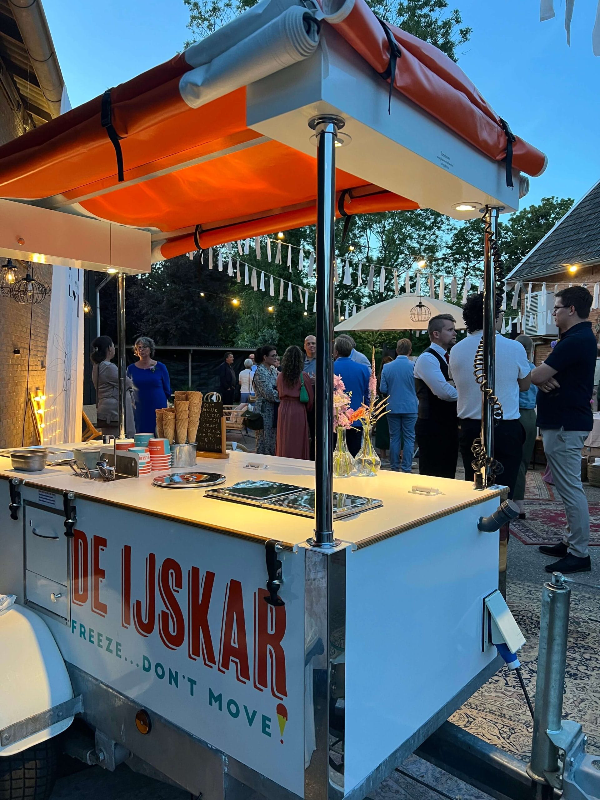 Gasten bij de ijskar op een bruiloft in de avond, met slingers en sfeerverlichting